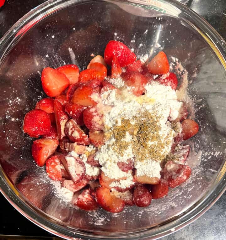 Strawberries with other filling ingredients, including flour and cardamom, in a large glass bowl.