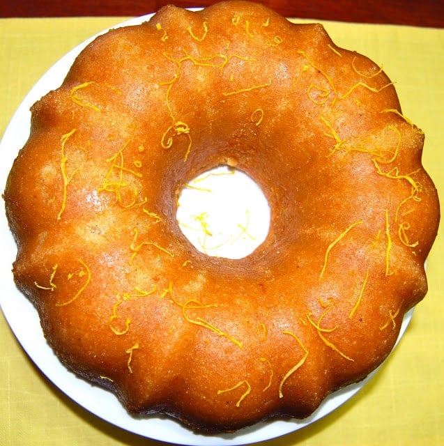 A lemon poppy seed bundt cake decorated with lemon zest strands on a white plate.