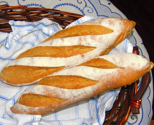 Whole wheat sourdough baguette loaves in blue and white napkin in straw basket.