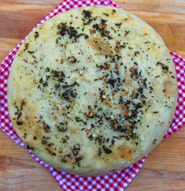 Photo of a round, herb-studded, crusy ciabatta bread loaf.
