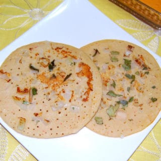 Two pieces of brown rice uthappam in white plate.