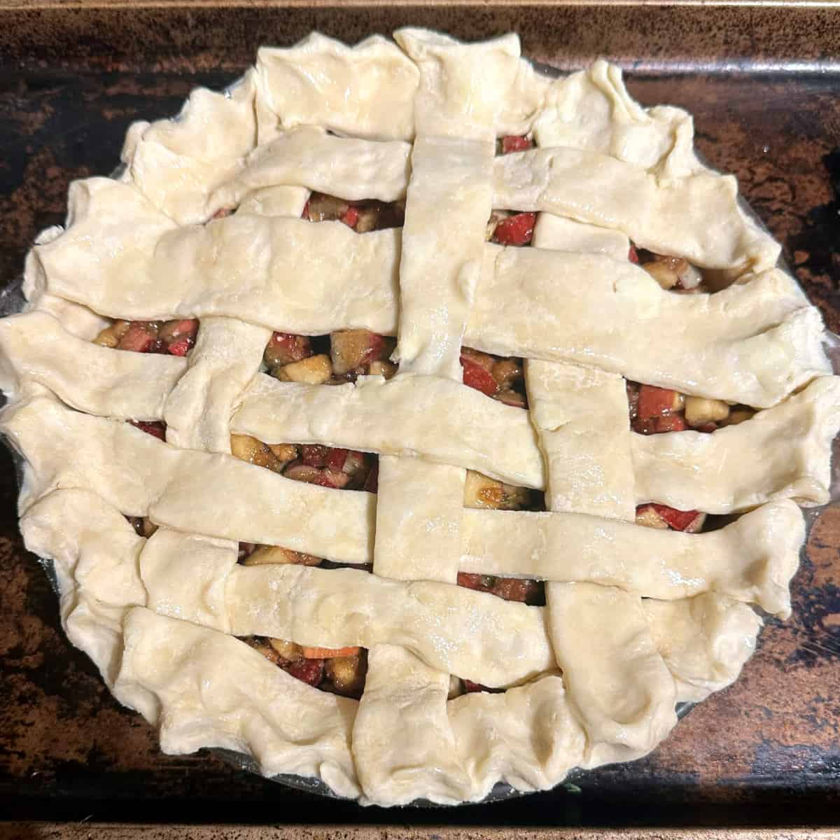 Rhubarb pie with lattice crust on baking sheet before baking.