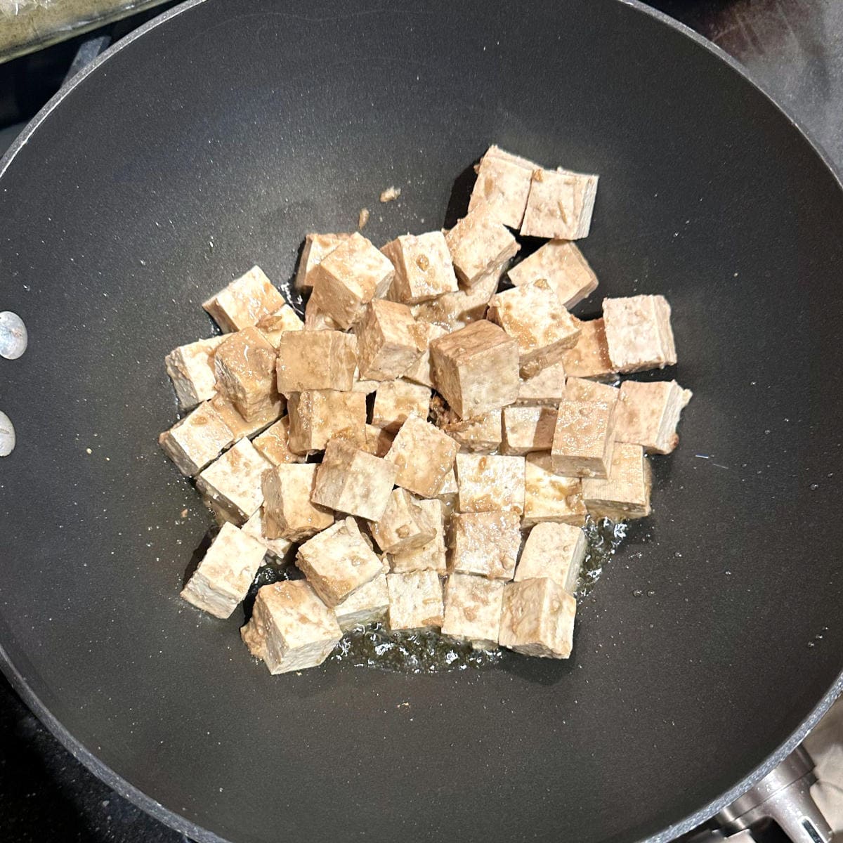Marinated tofu added to wok for frying.