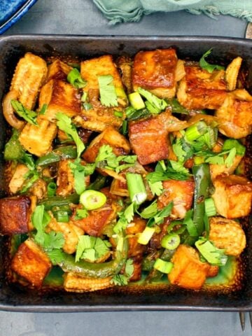Chilli tofu in a square bowl with scallions and cilantro.