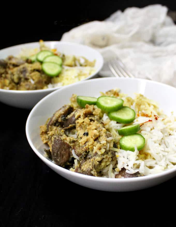 Vegan Mushroom Biryani in white bowls with cucumber slices and forks.
