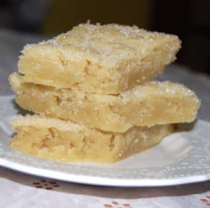 Three pieces of vegan coconut shortbread stacked on white plate.