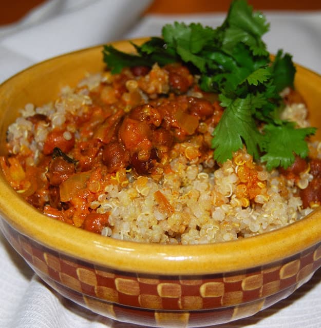 Quinoa biryani in yellow bowl with kala chana and cilantro garnish.