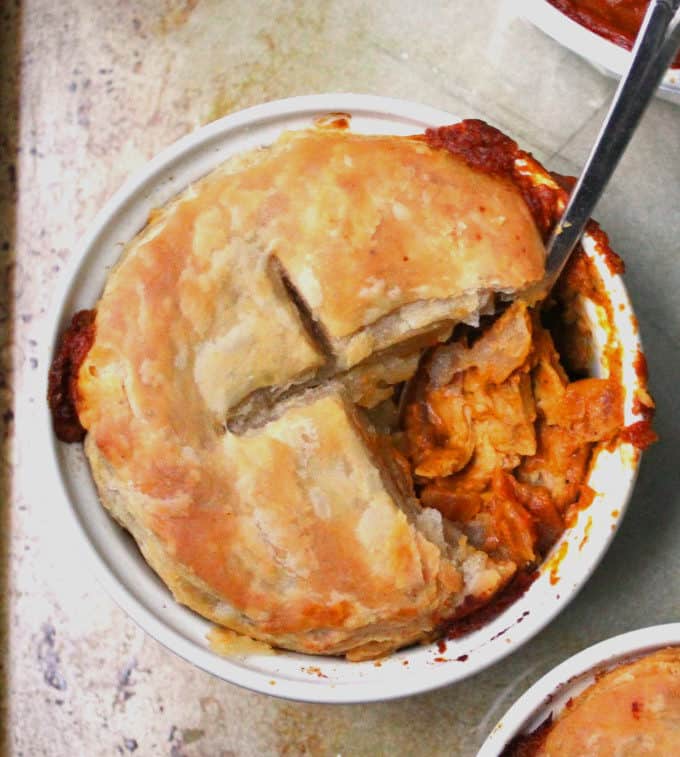 A close-up top shot of a golden, flaky chicken tikka masala pot pie with the tikka masala filling showing and a spoon