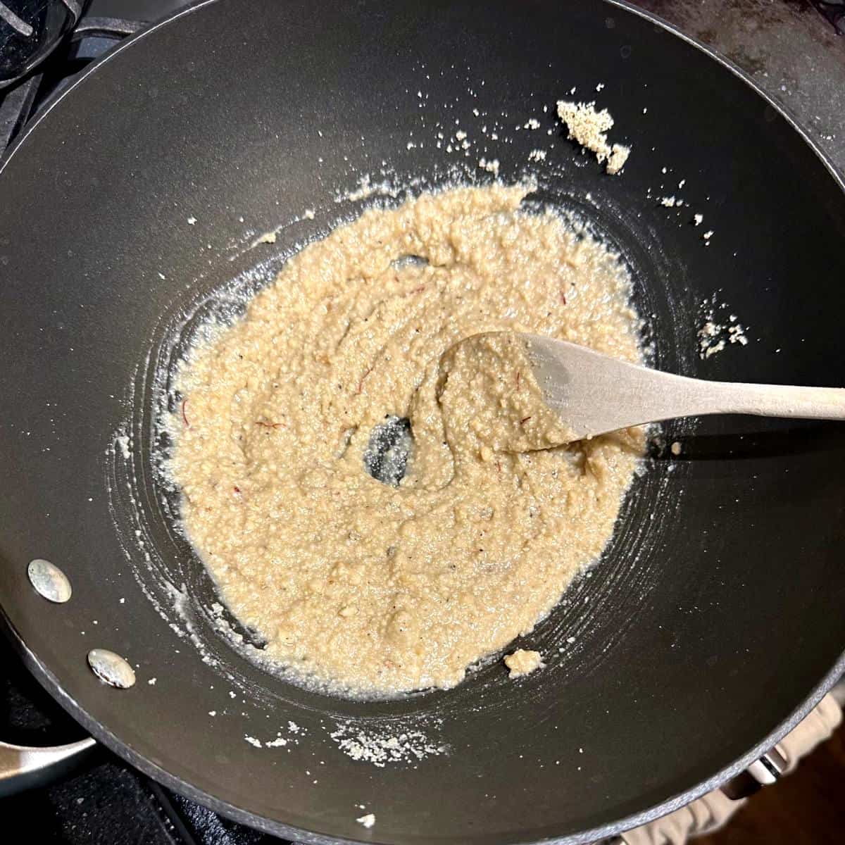 Sugar syrup added to cashew powder in wok.