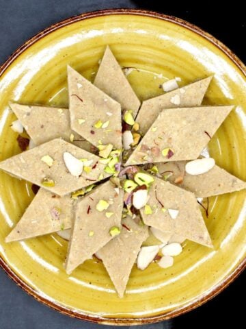 Vegan kaju katli on yellow plate with nuts and saffron.