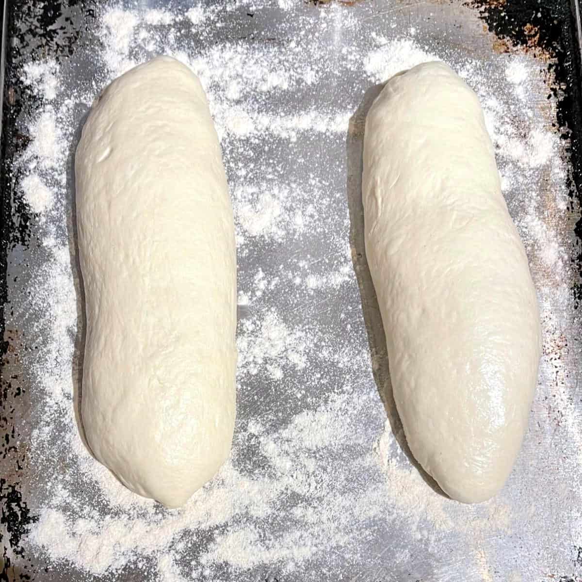 Italian bread loaves on baking sheet before rising.