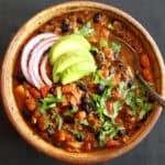 A bowl of vegan slow cooker chili with onions, avocado and cilantro.