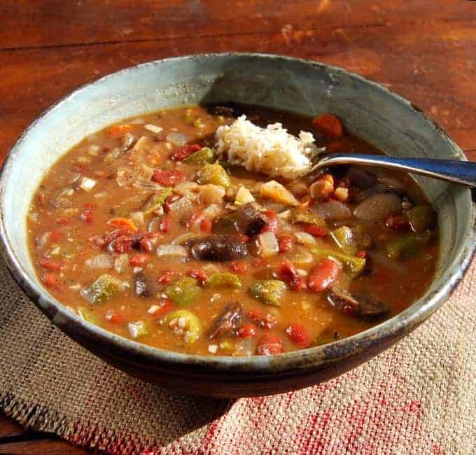 Photo of a large bowl of vegan gumbo that's also gluten free, served with brown rice on a wooden table