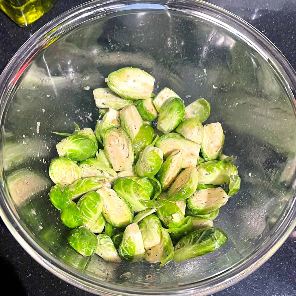 Brussels sprouts tossed with oil and seasonings in bowl.