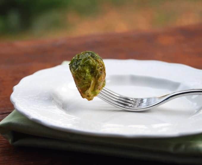 A single roasted Brussels sprout speared on a fork over a white plate.