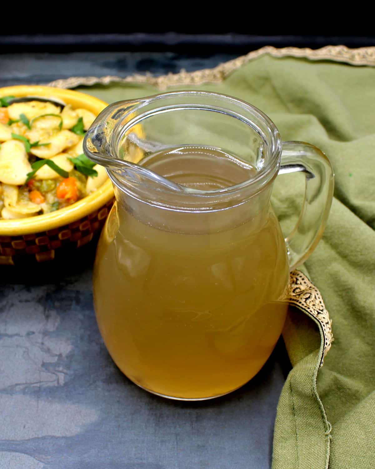 Vegetable stock in glass pitcher with a bean dish in background.