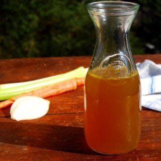 vegetable stock in glass bottle with veggies in background.