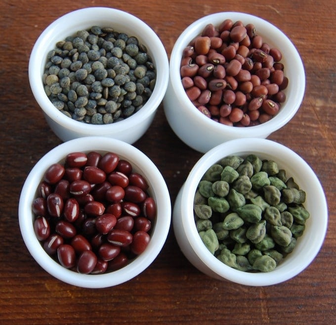 Beans of four different varieties in small white bowls.