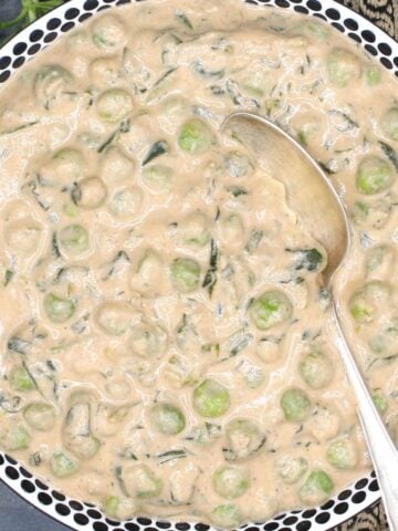 Methi matar malai in white bowl with black polka dots and a silver spoon.