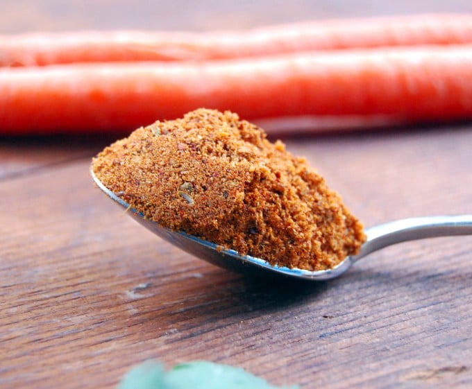 Photo of a spoon with berbere spice mix with carrots in background.