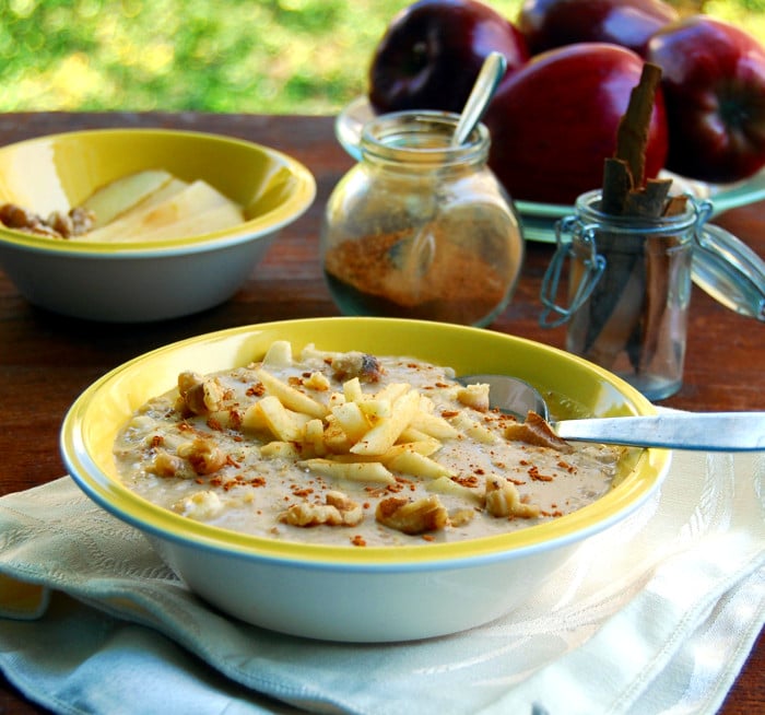 Apple Cinnamon Oatmeal in yellow bowl with apples, cinnamon and a napkin.