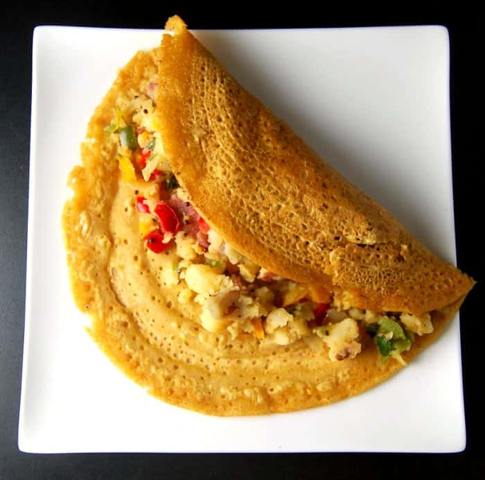 Photo of masala dosa folded in half with potato bell pepper sabzi on a white plate