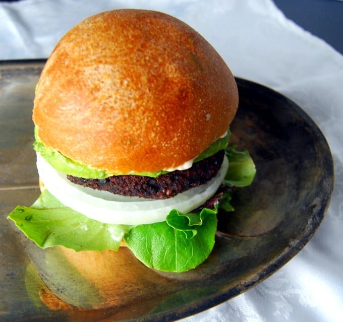 A Black Bean Black Rice Veggie Burger in a whole wheat hamburger bun on a silver tray.