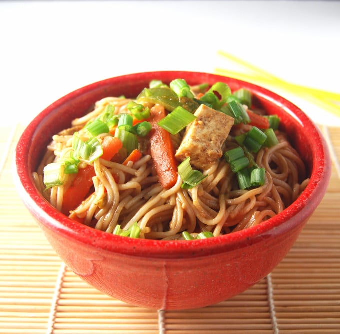 Photo of vegan Thai noodles with spicy peanut sauce, scallions, tofu and bell peppers in a red bowl.