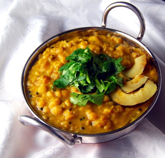 Front photo of Cholar Dal in a kadhai bowl with slivers of coconut and cilantro on a white napkin
