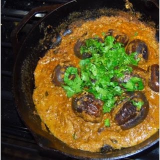 Baghare baingan in cast iron pan with cilantro garnish.