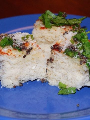 Brown rice dhokla with cilantro and mustard seed garnish on blue plate.