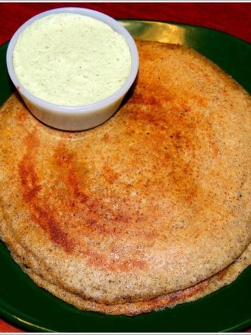 Brown rice dosa on green plate with a bowl of coconut chutney.
