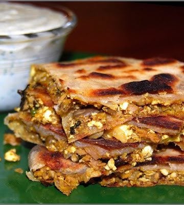 Vegan murtabak pieces with stuffing piled on green plate with raita in background.
