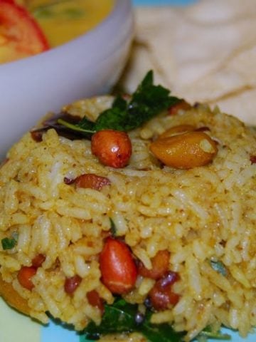Puliyodharai or tamarind rice with peanuts and aviyal in the background.