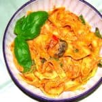 Bowl of pappardelle pasta in roasted tomato sauce with basil garnish.