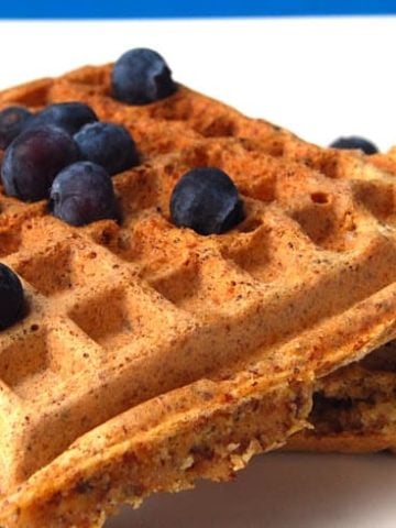 Vegan maple wheat germ waffles on white plate with blueberries.