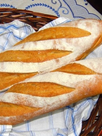 Whole wheat sourdough baguette loaves in blue and white napkin in straw basket.
