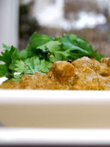 Vegan chicken curry with spinach in white plate with cilantro garnish.