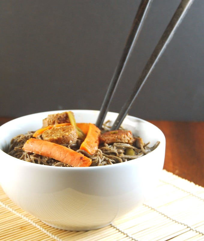 Vegan Black Bean Noodles with carrots and vegan sausage in white bowl with black chopsticks.