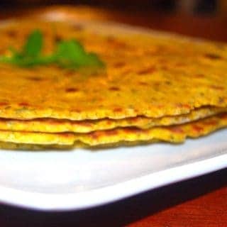 Stack of herb rotis on white plate with cilantro sprig on top.