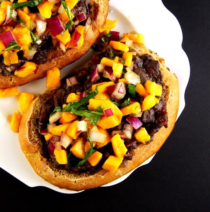 Molletes with refried beans and mango basil salsa on a white plate.