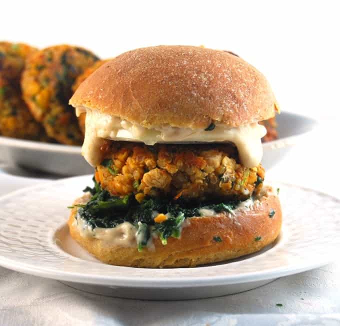 A Vegan Chickpea Quinoa Burger with creamy vegan mayo and greens on a white plate.