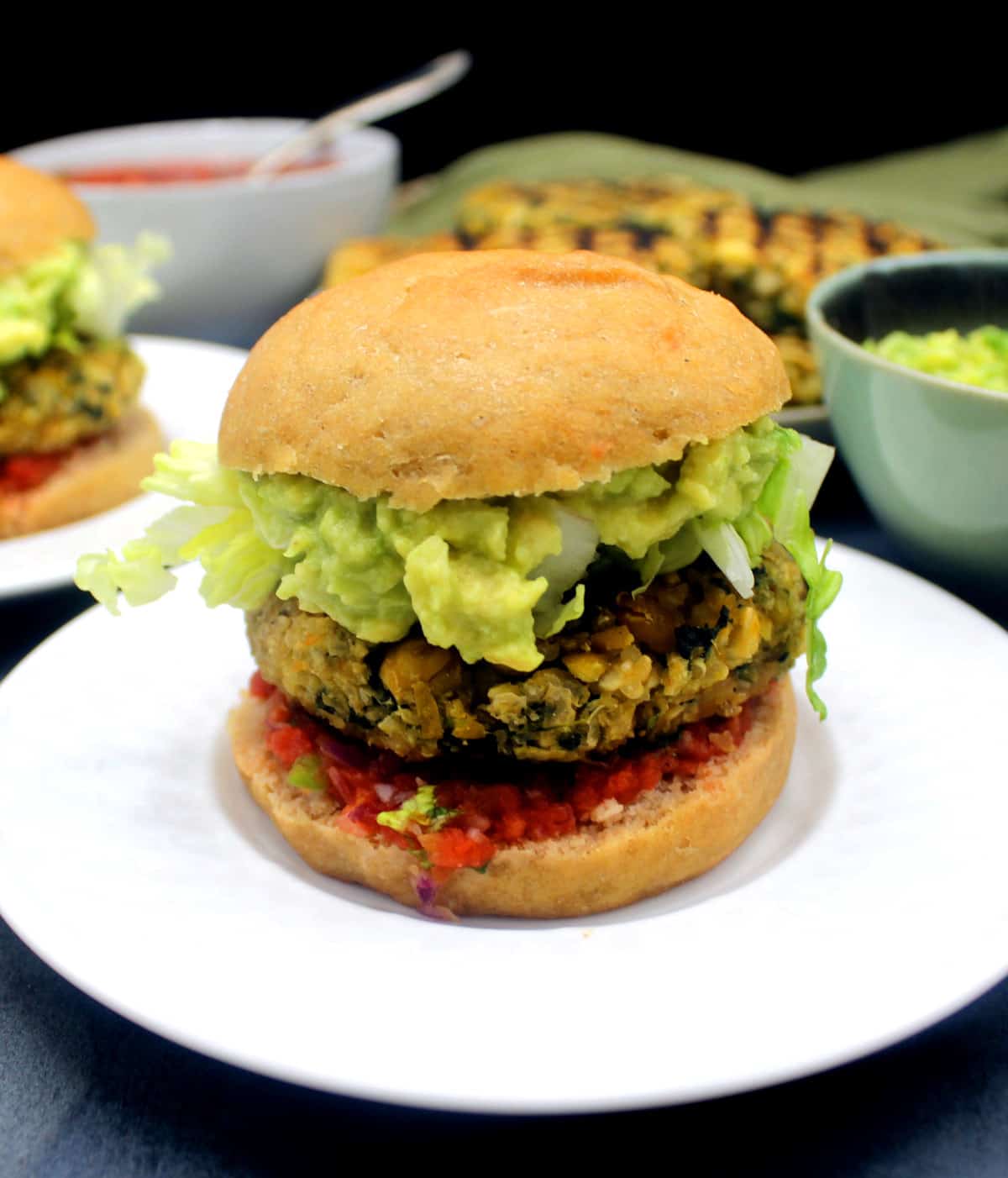 Vegan chickpea quinoa burger on white plate with toppings in background.