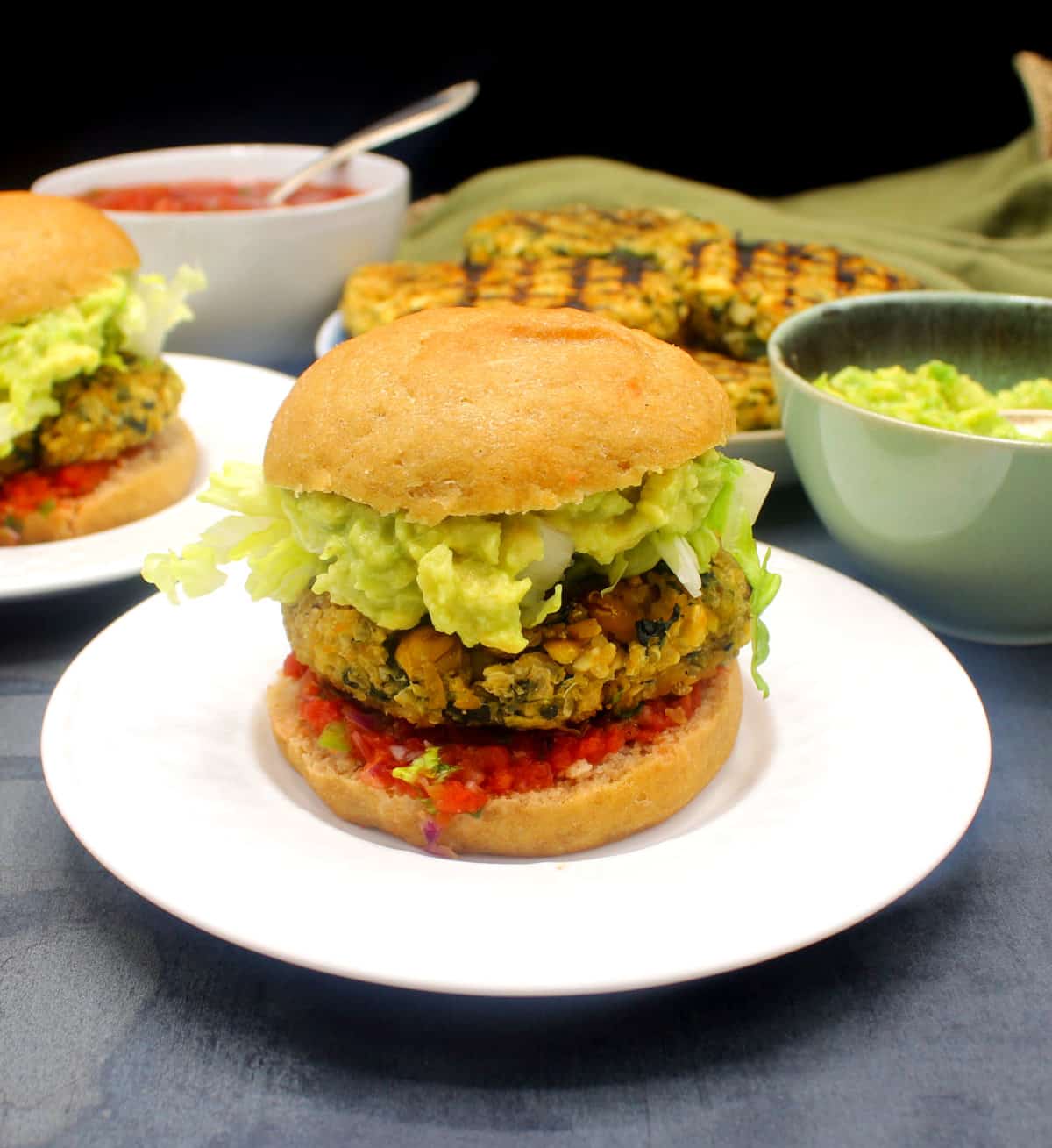 Vegan chickpea quinoa burger on white plate with trimmings in background.