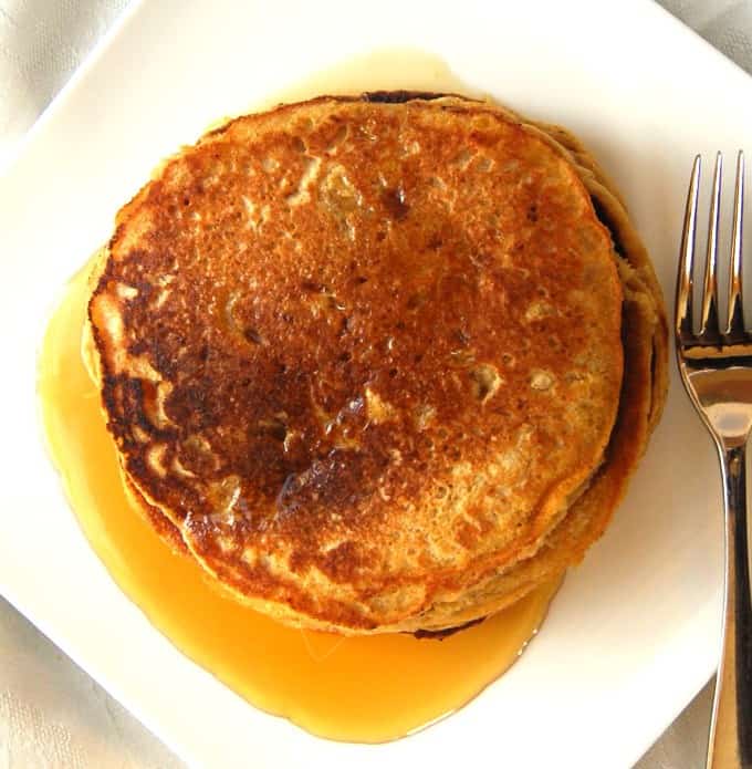 Sweet Potato Pancakes stacked on a white plate with maple syrup.