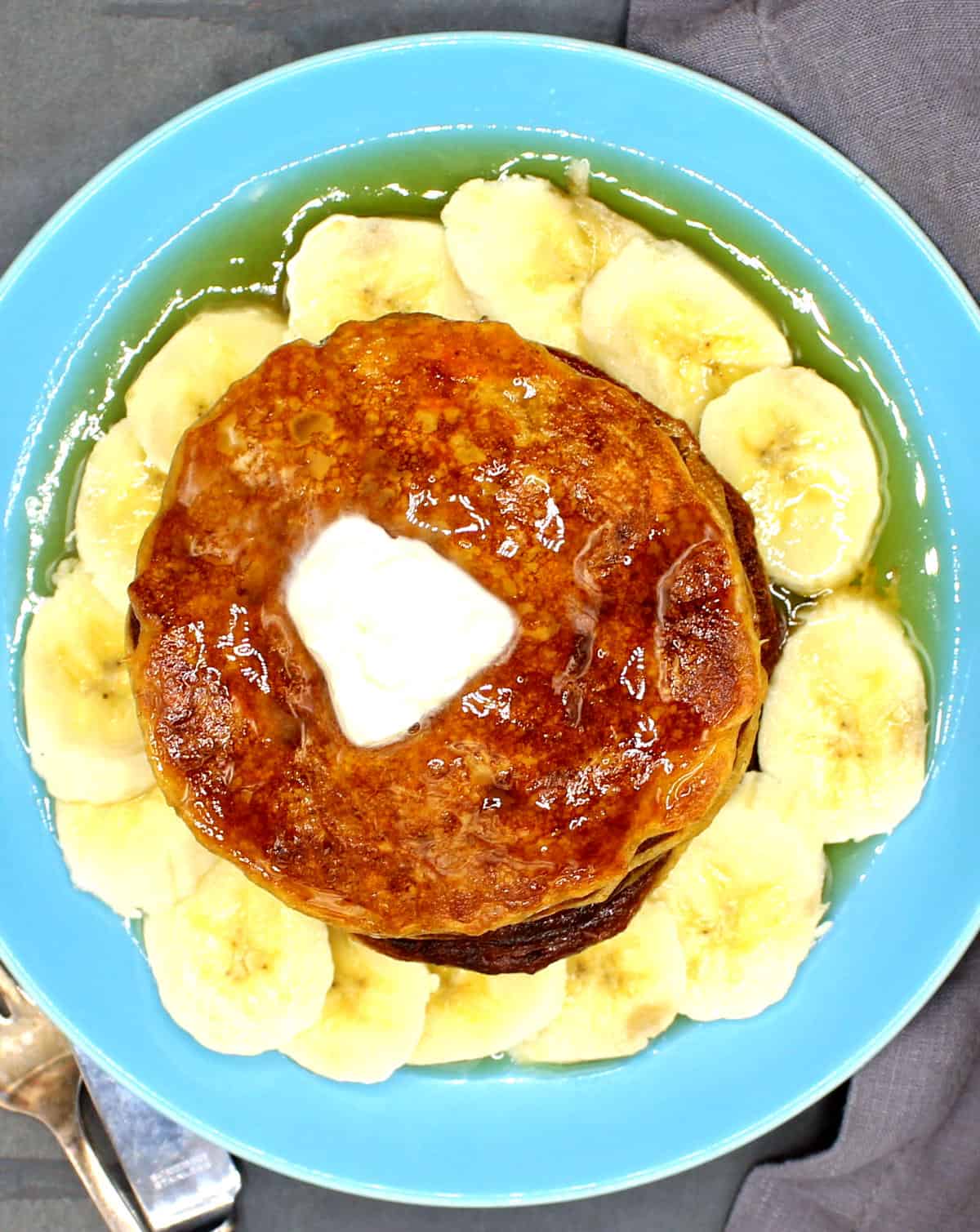 Vegan sweet potato pancakes with a pat of butter, maple syrup and slices of banana in blue plate.