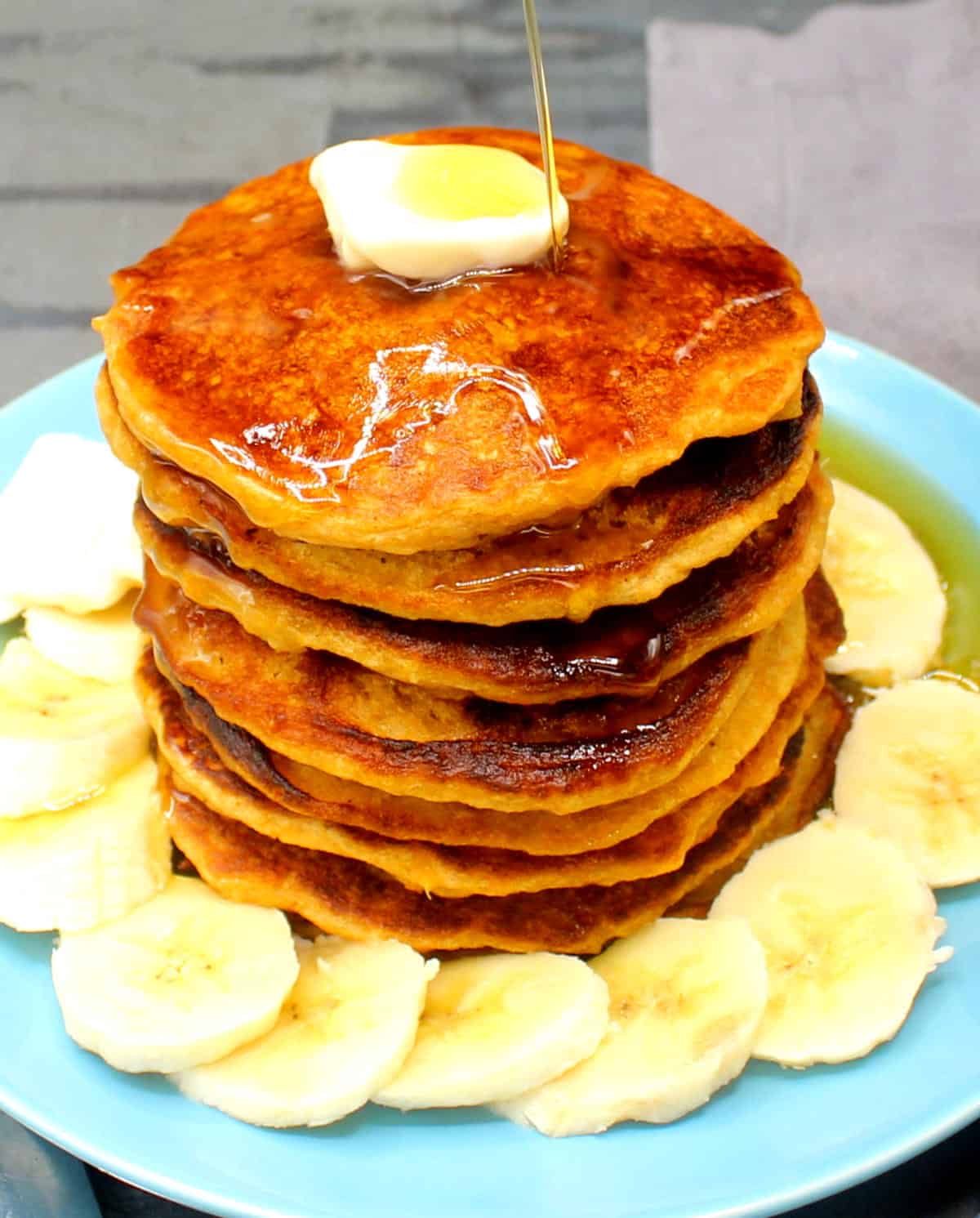 Vegan orange sweet potato pancakes stacked on blue plate with pat of butter and sliced bananas.