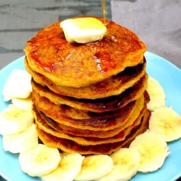 Vegan sweet potato pancakes stacked on blue plate with pat of vegan butter, maple syrup and sliced bananas.