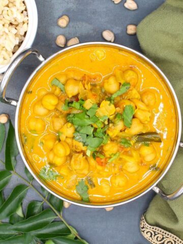 Chickpea Curry in karahi bowl with brown rice and chickpeas and curry leaves around it.