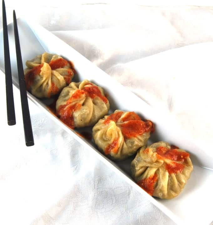 Vegan Momos in a white dish with chopsticks and red sauce